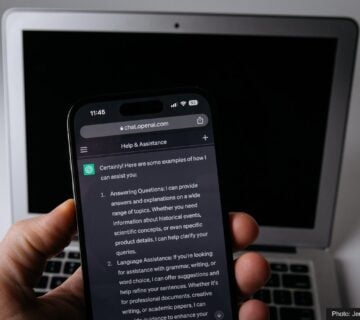 A hand holding a smartphone displaying ChatGPT in front of a laptop 